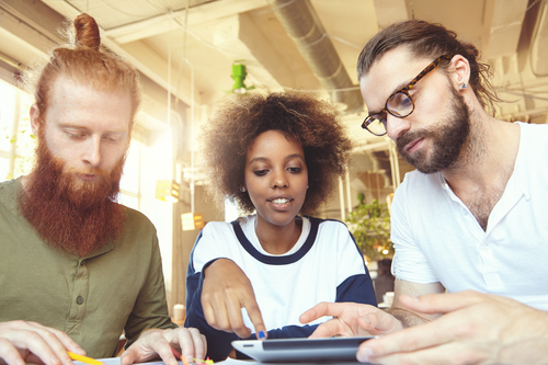 three-creative-people-having-discussion-cafe-african-woman-explaining-her-vision-pointing-screen-touch-pad-bearded-man-glasses-listening-attentively-redhead-partner-making-notes (1)
